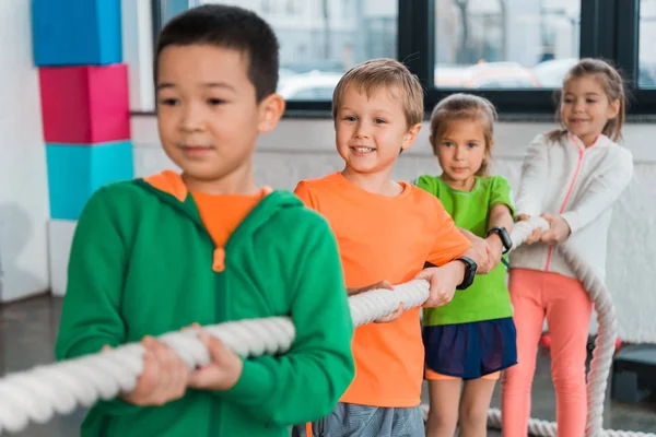 Selective focus of multiethnic children playing tug of war in sports center — Stock Photo