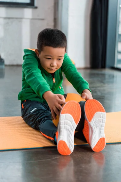 Asiatischer Junge hält Ball und dehnt sich auf Fitnessmatte im Fitnessstudio — Stockfoto