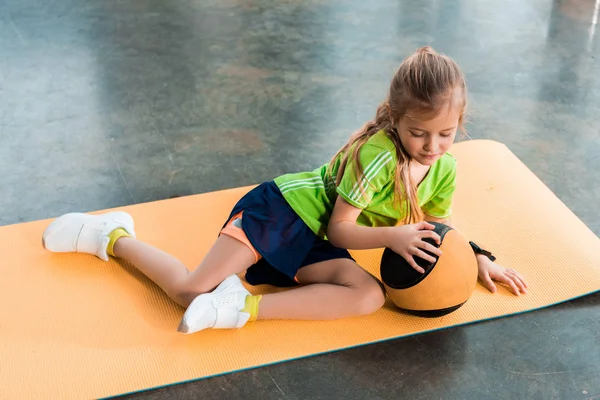 Kind berührt Ball und liegt auf Fitnessmatte in Turnhalle — Stockfoto