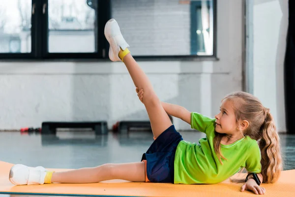 Enfoque selectivo del niño levantando la pierna mientras se estira en la estera de fitness en el centro deportivo - foto de stock