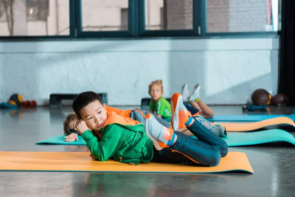 Selective focus of multicultural children resting on fitness mats in gym — Stock Photo