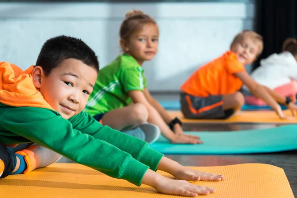 Selektiver Fokus multikultureller Kinder mit überkreuzten Beinen, die sich auf Fitnessmatten strecken — Stockfoto