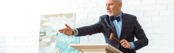 Panoramic shot of auctioneer holding gavel and pointing with hand during auction — Stock Photo