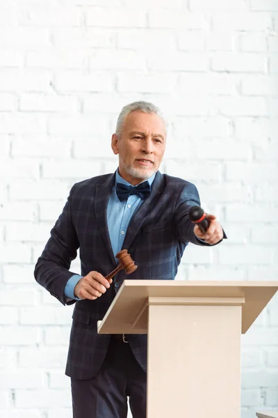 Auctioneer holding wooden gavel and microphone and pointing with finger during auction — Stock Photo