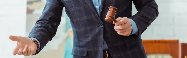 Panoramic shot of auctioneer holding wooden gavel and pointing with hand during auction — Stock Photo