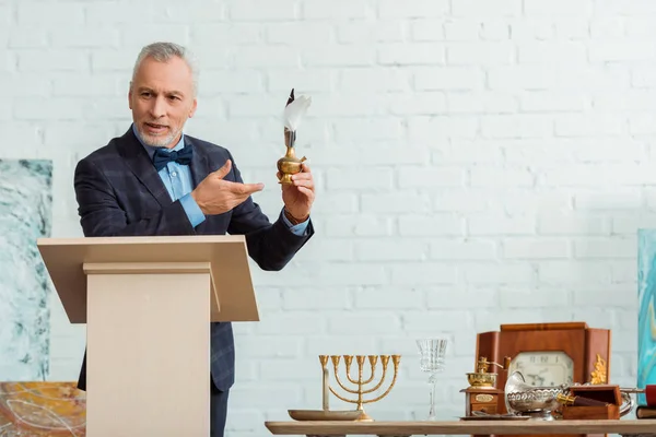 Handsome auctioneer in suit pointing with hand at feather pen during auction — Stock Photo