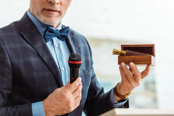 Обрезанный вид аукциониста разговаривающего с микрофоном и держащего коробку со шпионским стеклом во время аукциона — стоковое фото