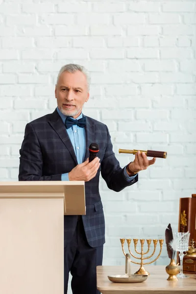 Handsome auctioneer in suit talking with microphone and holding spyglass during auction — Stock Photo