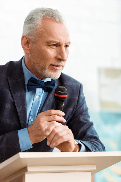 Beau commissaire-priseur en costume parlant avec microphone pendant la vente aux enchères — Photo de stock