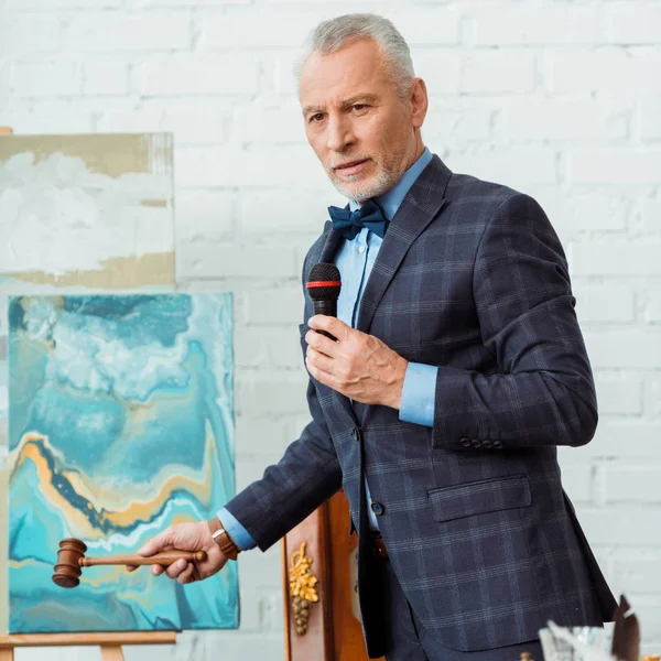 Auctioneer in suit talking with microphone and holding gavel during auction — Stock Photo