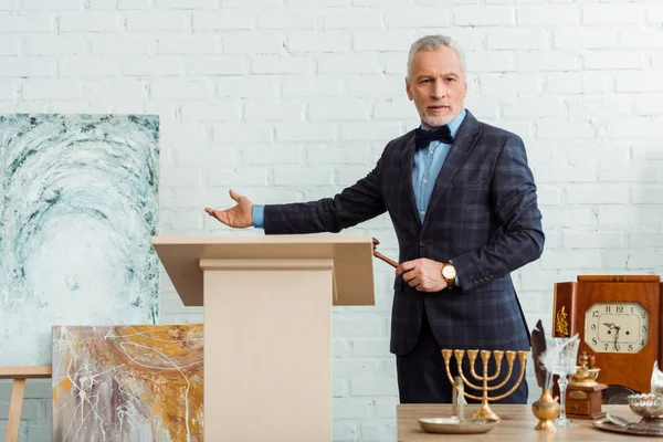 Auctioneer holding gavel and pointing with hand at picture during auction — Stock Photo