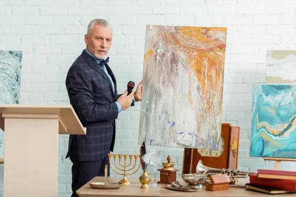 Auctioneer talking with microphone and standing near picture during auction — Stock Photo