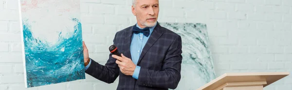 Panoramic shot of auctioneer talking with microphone and holding picture during auction — Stock Photo