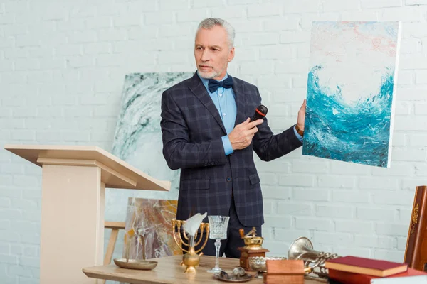 Auctioneer in suit with microphone holding picture during auction — Stock Photo