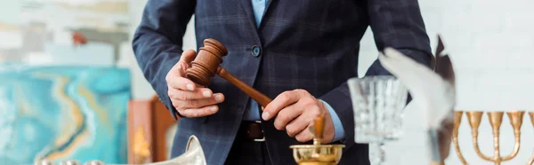 Panoramic shot of auctioneer in suit holding wooden gavel during auction — Stock Photo