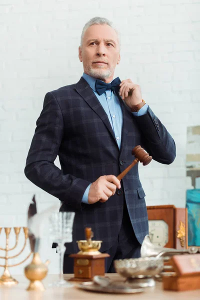 Selective focus of handsome auctioneer in suit holding gavel during auction — Stock Photo