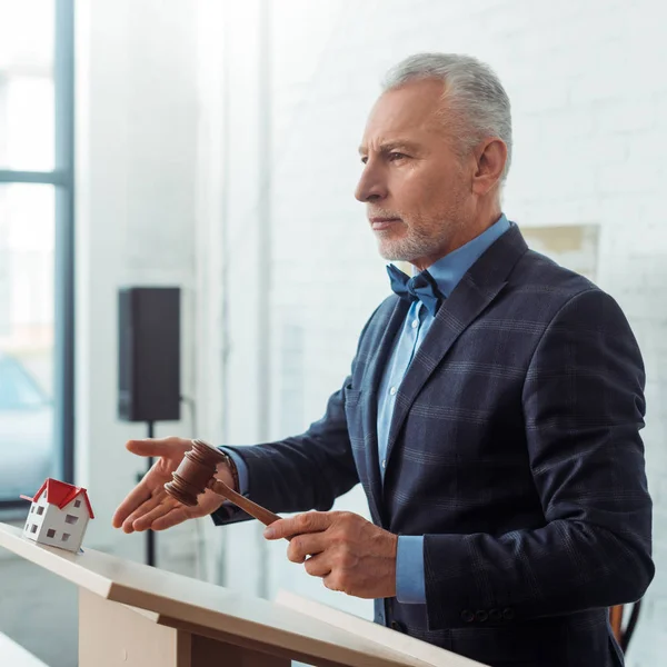 Auctioneer pointing with hand at model of house and holding gavel during auction — Stock Photo