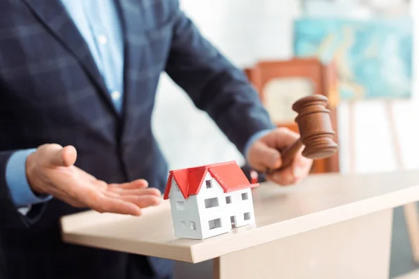 Ausgeschnittene Ansicht des Auktionators, der mit der Hand auf das Modell des Hauses zeigt und während der Auktion einen Hammer hält — Stockfoto