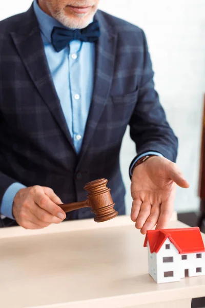 Cropped view of auctioneer pointing with hand at model of house and holding gavel during auction — Stock Photo