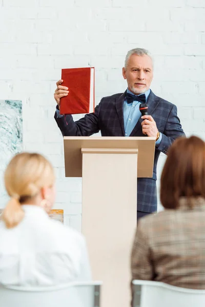 Selective focus of auctioneer talking with microphone and holding book during auction — Stock Photo