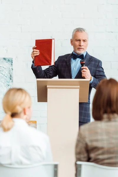 Foyer sélectif de l'encanteur parlant avec le microphone et le livre de holding pendant la vente aux enchères — Photo de stock