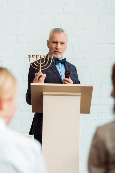 Selective focus of auctioneer talking with microphone and holding candlestick during auction — Stock Photo