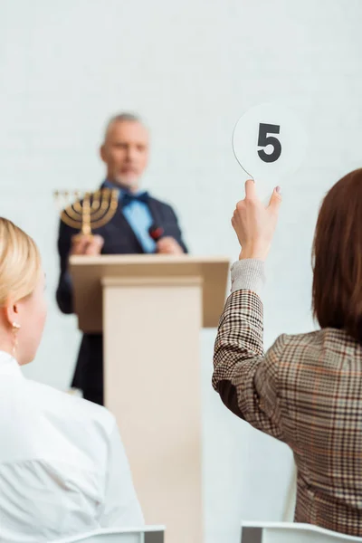 Back view of buyer showing auction paddle with number five to auctioneer during auction — Stock Photo