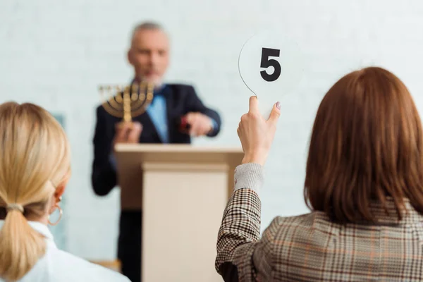 Back view of buyer showing auction paddle with number five to auctioneer during auction — Stock Photo