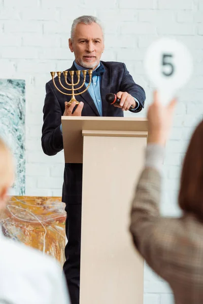 Selective focus of auctioneer looking at buyer and holding candlestick during auction — Stock Photo