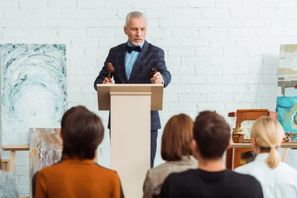 Selective focus of auctioneer holding gavel and microphone and looking at buyers during auction — Stock Photo