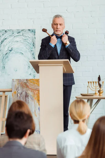 Selective focus of auctioneer holding gavel and microphone and looking at buyers during auction — Stock Photo