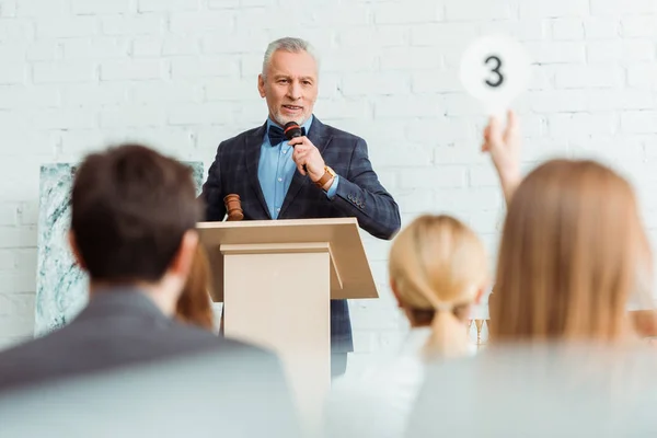 Selective focus of auctioneer talking with microphone and looking at buyer during auction — Stock Photo