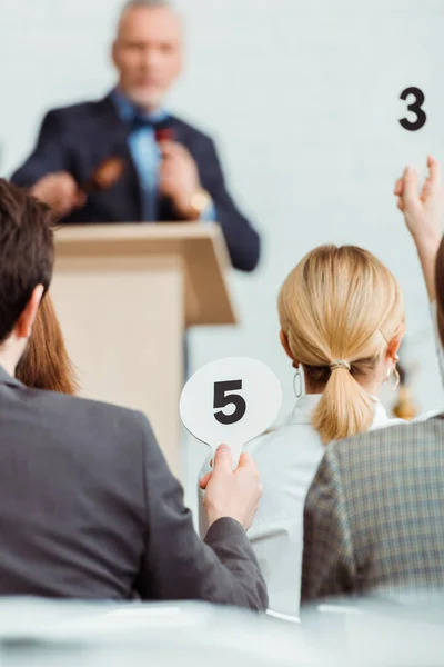 Back view of buyers showing auction paddles with numbers five and three to auctioneer during auction — Stock Photo