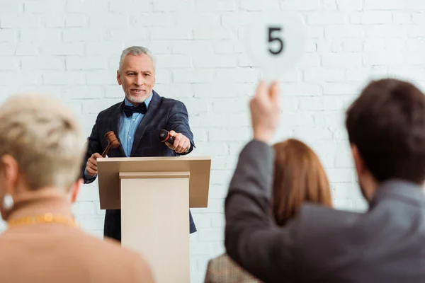 Selective focus of smiling auctioneer pointing with finger at buyer during auction — Stock Photo