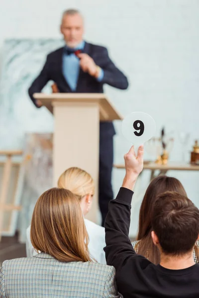 Back view of buyer showing auction paddle with number nine during auction — Stock Photo