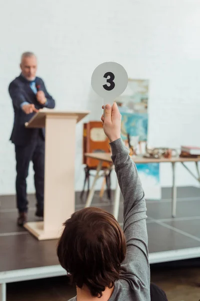 Vue arrière de l'acheteur montrant la pagaie d'enchère avec le numéro trois à l'encanteur pendant la vente aux enchères — Photo de stock