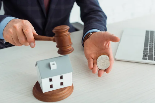 Cropped view of auctioneer hitting model of house with gavel and holding coins — Stock Photo