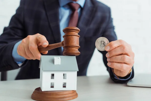 Cropped view of auctioneer hitting model of house with gavel and holding coins — Stock Photo