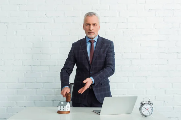 Auktionator hält Hammer in der Hand und zeigt mit der Hand auf Hausmodell — Stockfoto