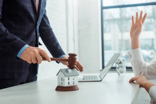 Ausgeschnittene Ansicht eines Auktionators, der mit einem Hammer auf ein Modell des Hauses einschlägt und eine Frau, die die Hand hebt — Stockfoto