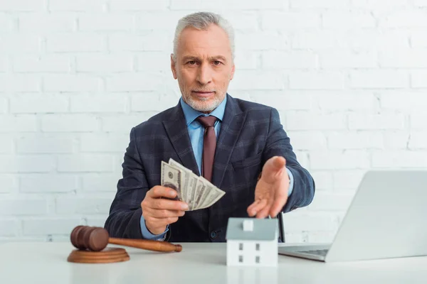 Auktionator zeigt mit der Hand auf Hausmodell und hält Dollarnoten in der Hand — Stockfoto