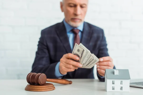 Selective focus of gavel and model of house and auctioneer holding money on background — Stock Photo