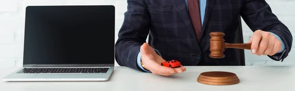 Panoramic shot of auctioneer holding gavel and model of car near laptop — Stock Photo