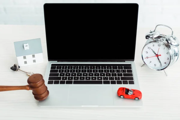 Wooden gavel, models of car and house, key, laptop, alarm clock on table — Stock Photo