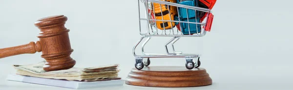 Panoramic shot of gavel, money, shopping trolley with models of cars on white background — Stock Photo