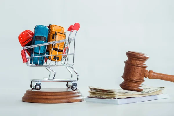 Gavel, money, shopping trolley with models of cars on white background — Stock Photo