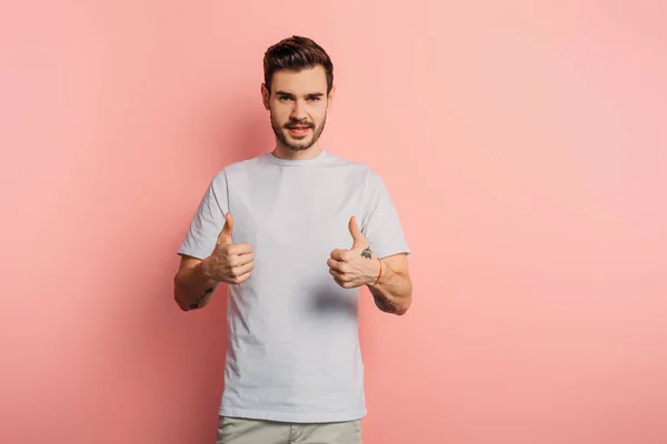 Lächelnder schöner Mann zeigt Daumen nach oben, während er in die Kamera auf rosa Hintergrund schaut — Stockfoto