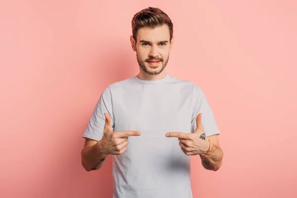 Smiling handsome man showing gun gestures while looking at camera on pink background — Stock Photo