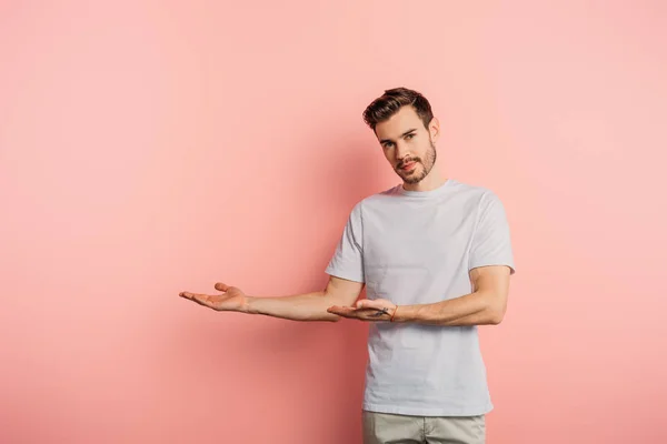Schöner selbstbewusster Mann, der mit den Händen zeigt und auf rosa Hintergrund in die Kamera schaut — Stockfoto