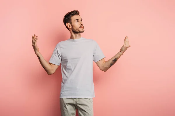 Dreamy young man looking up while standing with open arms on pink background — Stock Photo